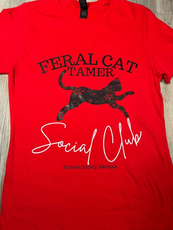 Bright red t-shirt featuring "Feral Cat Tamer Social Club" text with a decorative black cat silhouette and "Bartow County, Georgia" branding