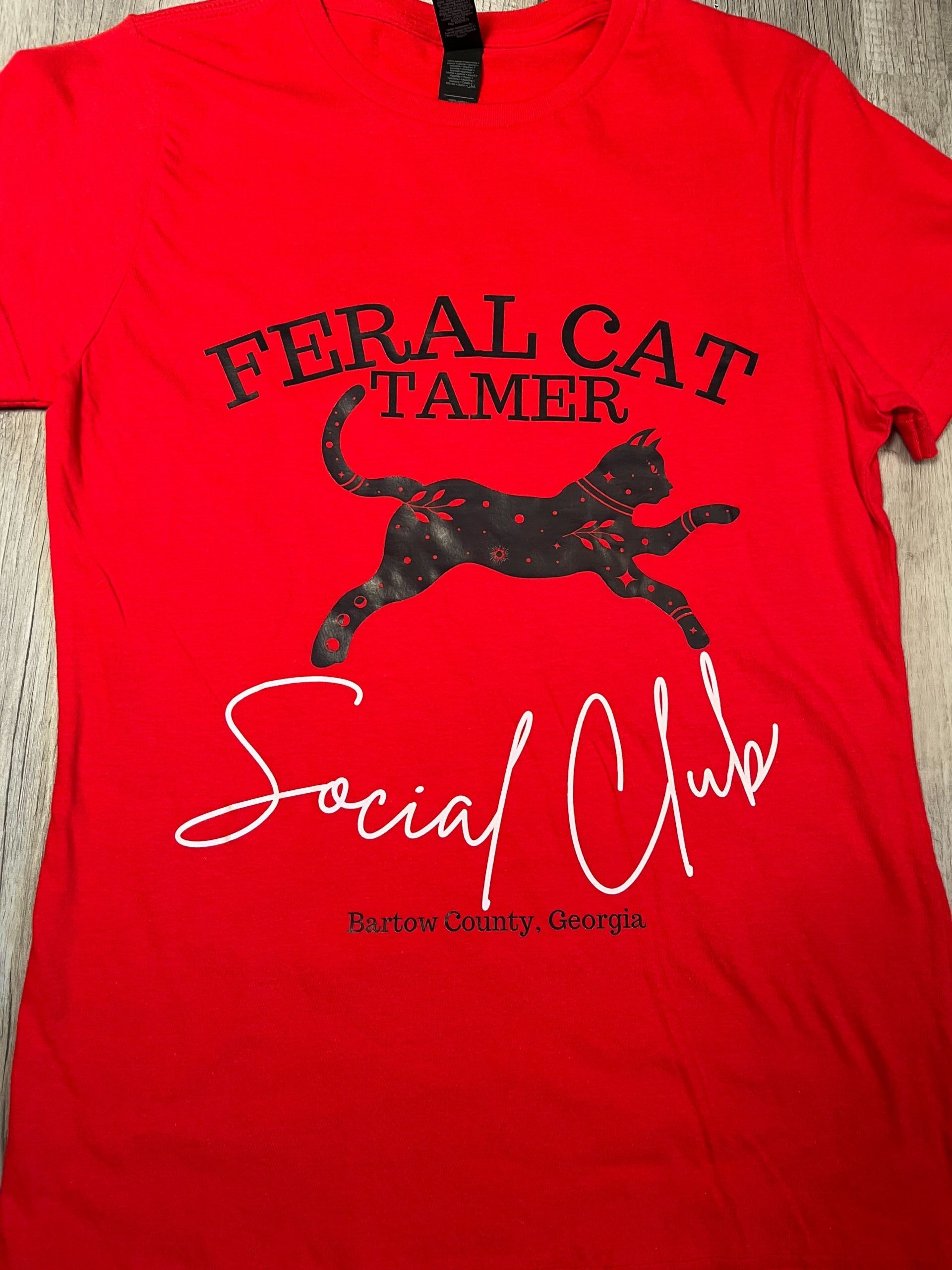 Bright red t-shirt featuring "Feral Cat Tamer Social Club" text with a decorative black cat silhouette and "Bartow County, Georgia" branding